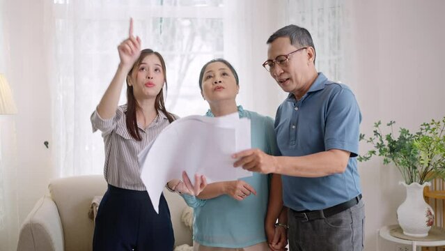 Asian mature couple thinking about buying real estate.Happy senior old aged woman and man customer landlord hold key to new house apartment,signing contract deal of loan pension mortgage at home.