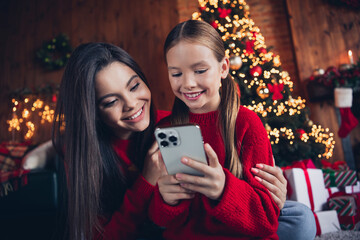 Photo of adorable sweet little siblings dressed red sweaters ordering gifts apple iphone device indoors christmas apartment home