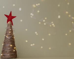 Small Christmas tree made of a bundle with a felt red star and garland lights on a beige background