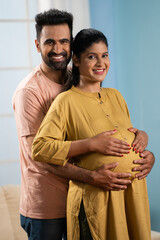 vertical Portrait shot of happy indian Pregnant woman with husband looking at camera while talking...