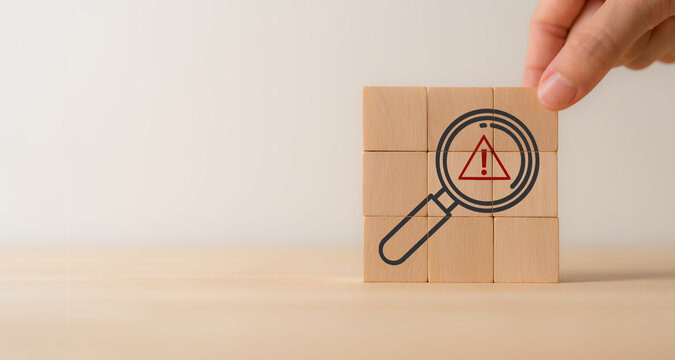 Risk analysis and management concept. Identify potential risks and develop strategies to mitigate. Wooden cube blocks with magnifying glass and triangle caution warning sign. VUCA management concept.