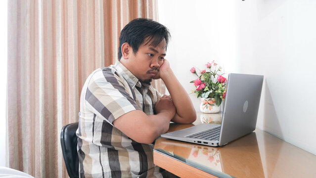 Indonesian man looking at laptop with disapproved and grumpy expression.