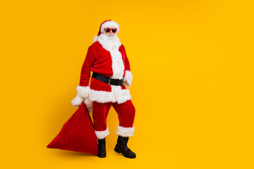 Full body photo of aged santa claus hold new year gifts bag empty space ad isolated on yellow color background
