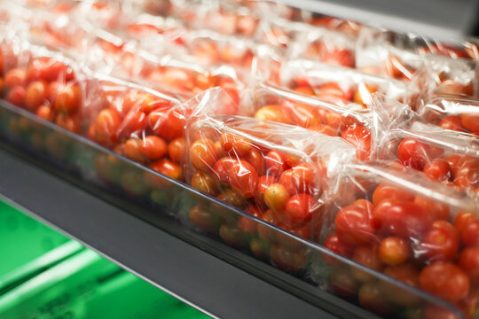 Cherry tomatoes in plastic container. Supermarket shelf with vegetables. Plastic foil vegetable wrap. Packed tomatoes background. Cherry tomatoes box on market shelf.
