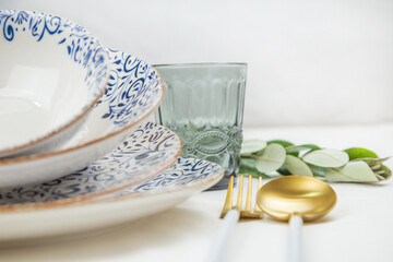 On the side there is a set of plates of different sizes with a white middle and blue patterns on the side of the plate and a gold border, they stand on top of each other with a tilt, there are gold -