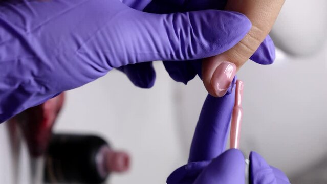 A vertical close up of manicurist applying pink polish to a woman's nails in a nail salon
