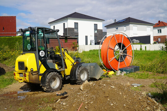 Roll of orange fiber optic cable for faster Internet in rural regions. Yellow digger for laying the underground cable in the soil. Barsinghausen, district of Hanover, Germany.