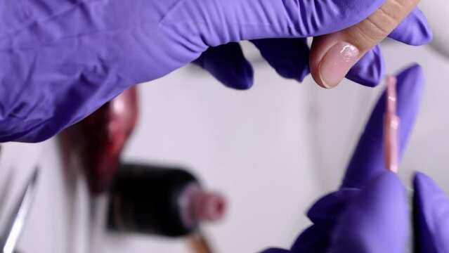 A vertical close up of manicurist applying pink polish to a woman's nails in a nail salon