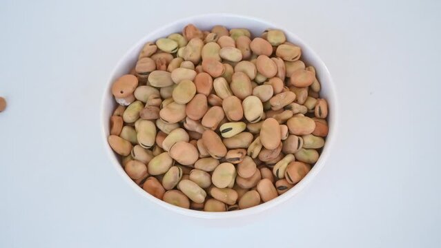 Dried fava beans falling in a white plate on a white background