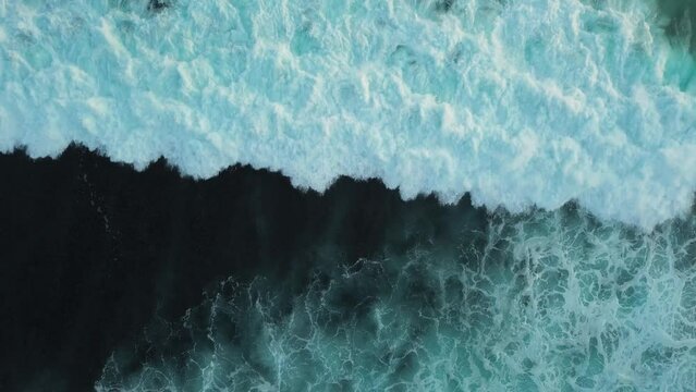 Background video, meditation, and relaxation. Aerial view of the ocean and huge waves that fall on the surface of the water and create foam. Blue endless ocean and surfing waves.