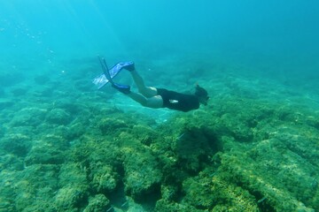 Girl snorkeling, skin diving and swimming with fins in the green blue sea, over the seabed....