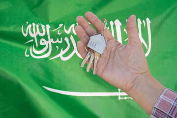 Keys to the apartment in a female hand on background of flag Saudi Arabia