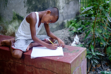 South asian primary school going student reading and writing in a white notebook sitting in front...