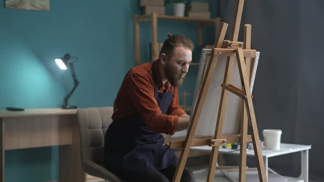 Handsome male painter is painting a modern abstract painting on a canvas and enjoyed favorite hobby