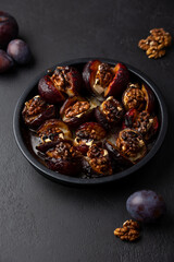 Plums baked with Camembert cheese, walnuts and honey on a black plate. Popular hot appetizer. Selective focus, close-up.