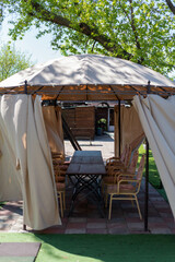 Street gazebo with a dome and light-colored curtains under a tree in a cafe