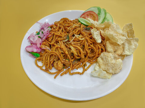 A typical aceh fried noodle called Mie Aceh, with lemon slices, tomatoes, cucumbers, shallots, shrimp, squid slices, chilies and Gnetum gnemon crackers
