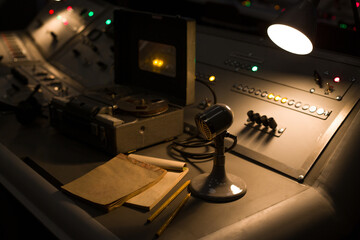 Vintage microphone on a control panel with buttons and toggle switches next to a notepad. Old...