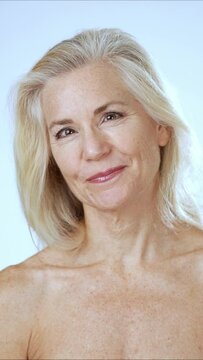 Vertical video portrait of smiling happy mature, senior, fit nude woman with gray blonde hair looking at camera isolated studio on white background.