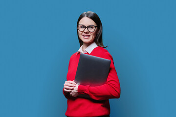 Portrait of young business woman holding laptop, on blue background