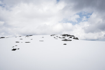 Perfect white snow on the mountain, against the black rocks and plants, on Kopren summit, under a moody, cloudy sky during winter - 683864602