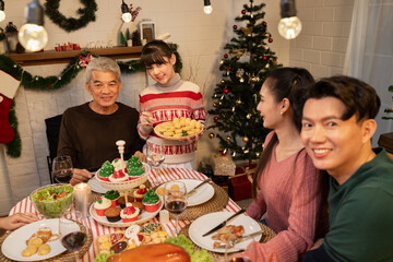 Happy Asia girl holding food with family celebrating Christmas in dinner at home