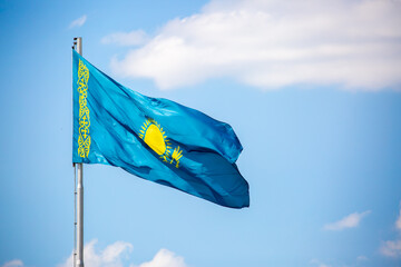 The flag of Kazakhstan is fluttering in the wind against the blue sky. The flag is located on the blue dome of the administrative building. The city of Astana is the administrative center.