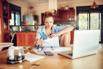 Concerned young woman reading through bank statements at home