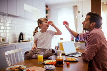 Overjoyed father and little daughter make funny faces with vegetable during breakfast