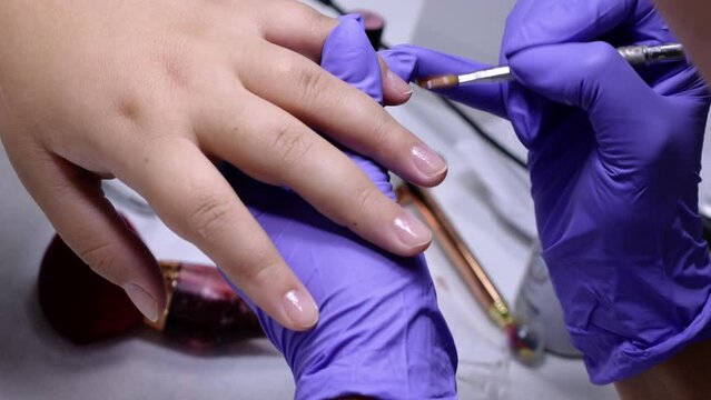 A vertical close up of manicurist applying a top coat to a woman's nails in a nail salon