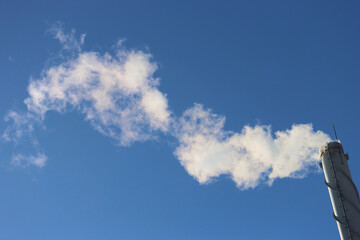 A chimney from a boiler room with white smoke against the background of a blue, sunny, clear sky.
