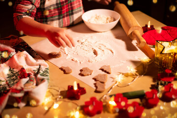 Children's hands covered in flour prepare Christmas cookies against the background of a festively decorated table.