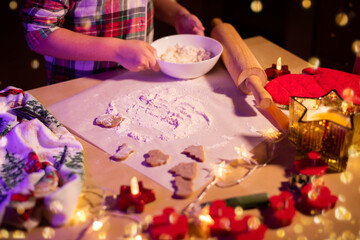 Children's hands covered in flour prepare Christmas cookies against the background of a festively decorated table.