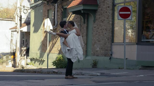 Husband carrying bride in wedding dress across screen in arms - wide shot - side profile