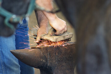 close up of hands of a farrier workingh on a glowing red hot horse shoe and on an anvil