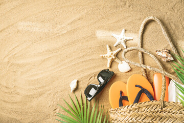 Woman's beach accessories bag, straw hat, flip flops, shells, sunglasses, palm leaves on sand...