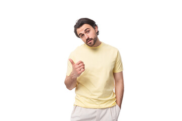 Fototapeta premium young brutal brunette man in a T-shirt points his hand to the side on a white background with copy space