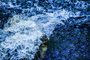 Water droplets / watercourse with reflections in the sunlight. Wonderful play of colours in small drops of water in a stream in the sun. Close-up taken in sunshine on the bank.