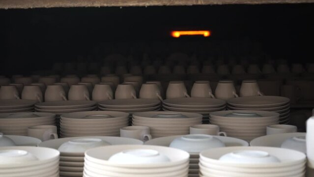 Blanks of ceramic plates on pallets entering the muffle kiln for firing at the porcelain factory.  Ceramic white mugs are fired in a muffle furnace at high temperature at a porcelain factory
