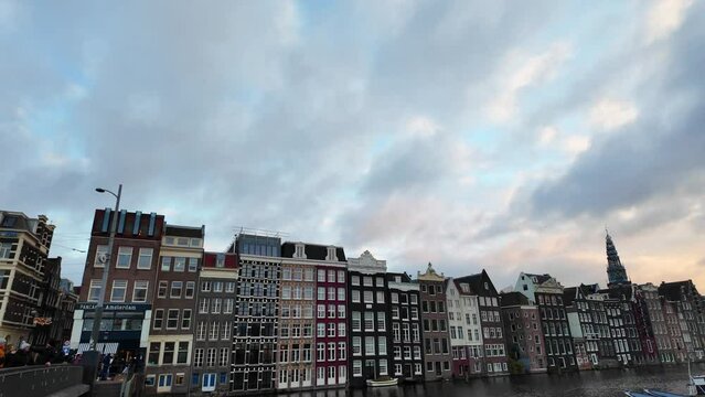 Amsterdam center historic houses at Damrak along the canal behind Warmoesstraat at sunset with beautiful sky, boats in the water, steady gimbal tilt down shot