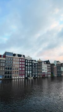 Amsterdam houses at Darmrak along the canal behind Warmoesstraat, during sunset with beautiful sky, boats in the water, gimbal panning vertical video