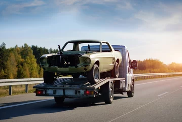 Deurstickers A Towing Truck In Motion With A Damaged Car After The Traffic Accident On A Road. Emergency Roadside Assistance. Retro Car Project Renovation. Vintage Car Recovery And Reanimation. © Andriy Sharpilo
