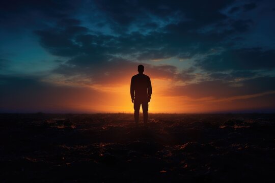 A man standing in the middle of a field at sunset. This image can be used to depict solitude, contemplation, or the beauty of nature