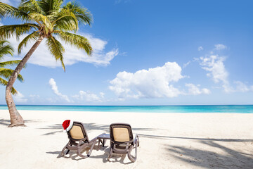 Santa Claus hat on sunbed near coconut palm tree on bounty and pristine beach on caribbean island....