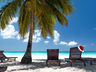Santa Claus hat on sunbed near coconut palm tree on bounty and pristine beach on caribbean island....