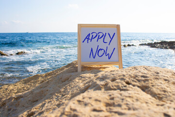Apply now symbol. Concept word Apply now on white chalk blackboard. Beautiful sea background....