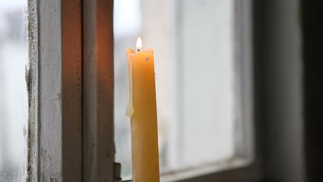 A burning wax candle burns on a windowsill in an old house.
