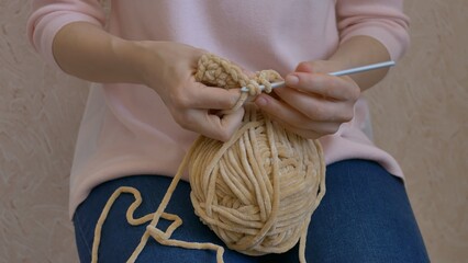 Woman crochets with beige yarn on knees, showcasing hobby. Crocheting as a hobby highlighted, ball...