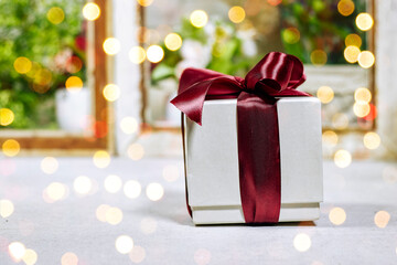 christmas and new year background - gift box near window show a garden and light bokeh