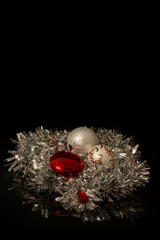 White and red Christmas baubles nested in a silver Christmas tinsel on a black background